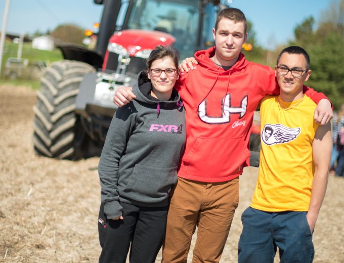 Deux étudiants accompagnés d'une étudiante de Gestion et technologies d'entreprise agricole prennent la pose dans un champ devant un tracteur